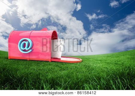 Red email postbox against green field under blue sky