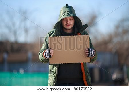 Homeless person with blanck cardboard. Focused on cardboard