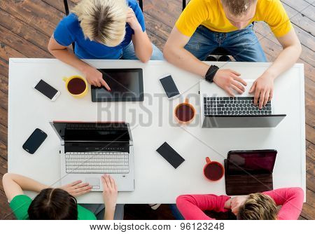 Students sitting at the table using computers and tablets.