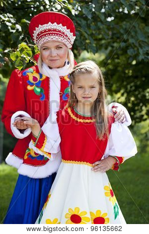 Portrait of mother and daughter in a national Russian costume on a background of green summer park