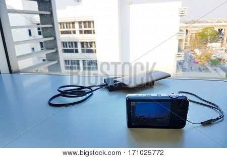 Compact digital camera on a white table with a city landscape background,Focus on holding camera capture a city landscape,Copy space,Vintage style,Low light style,photographer camera,photographer