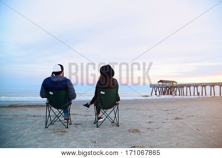 Couple Sitting In Deck Chairs At Beautiful Sunset Beach