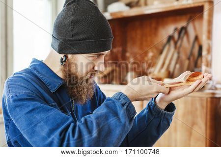 A portrait of man with a beard wearing blue jeans suit and black hat holding and looking at wooden spoon, woodcarving, portrait, copy space.
