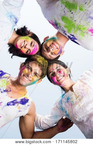 young Indian happy friends or couples with heads together in circle celebrating holi festival, with faces coloured with gulal