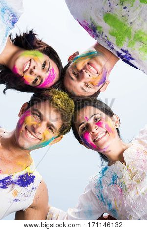 young Indian happy friends or couples with heads together in circle celebrating holi festival, with faces coloured with gulal