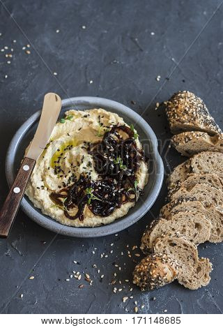 Balsamic caramelized onion hummus and whole wheat multi seed baguette on a dark background. Delicious vegetarian snack