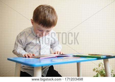 little boy sitting at the desk and reading a book.