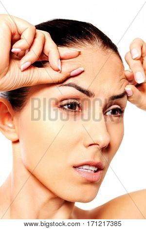 Worried young woman checking wrinkles on forehead