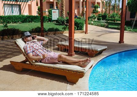 man in a hat lying on a lounger and talking on the phone.