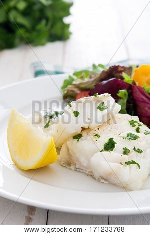 Fried cod fillet and salad in plate on white wooden background