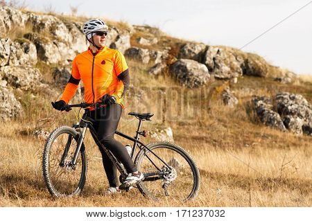 Cyclist Riding the Bike on the Beautiful Spring Mountain Trail. Cyclist in the helmet and the gkasses. Travel in the countryside. Beautiful landscape with hill and rock.