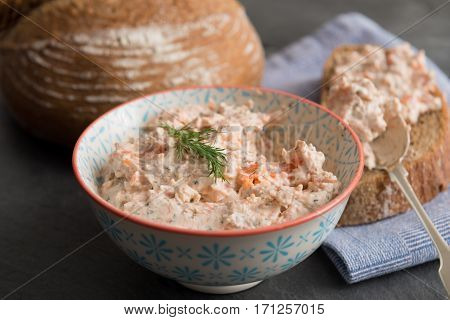 Bowl of fresh fish pate beside sliced bread and spoon with pate and round bread loaf