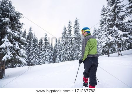 Hiker goes in snowshoes through the alpine meadow during snowfall - winter adventure in the mountains. Back view.