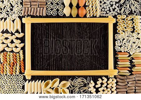 Assortment italian dry pasta on dark brown wooden board with blank copy space as decorative frame background.