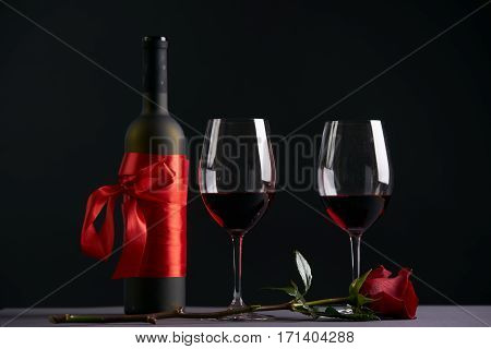 Wine bottle and two wineglasses with red rose on a dark background. Valentine's day theme concept