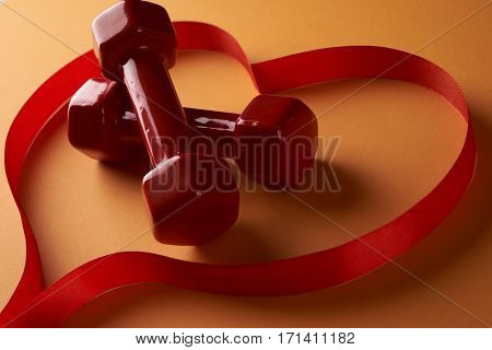 Red dumbbells and ribbon shaped as heart on a orange background Сardio workout concept