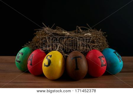 Easter holidays tradition and object concept - close up of colored easter eggs and quaill eggs in nest on wooden surface.black background