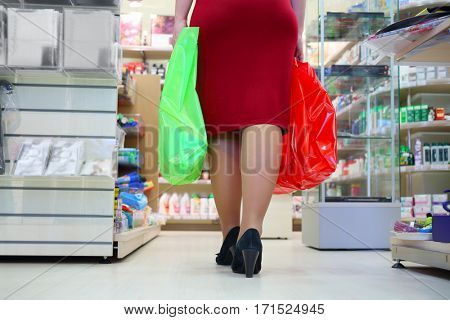 Woman in red with two bags in supermarket, back view, noface