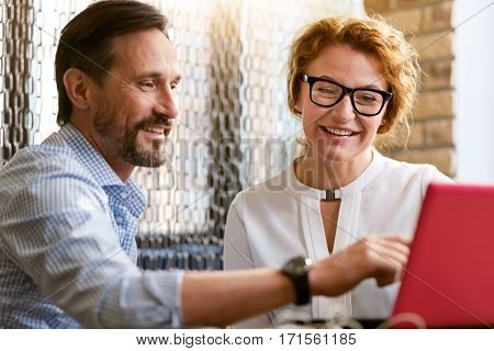 I have an idea. Positive involved cheerful colleagues sitting at the table in the cafe and working while discussing the project and looking at the laptop