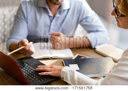 Discussing the project together. Involved friendly lively collaborators sitting at the table in the cafe and talking while using the laptop and making notes