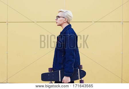 Profile photo of attractive female hipster with short haircut dressed in trendy casual street wear while practicing in sports activities with skateboard standing near copy space for your advertising