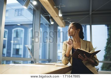 Skillful professional female thinking over organizing work in office and employee while being in business trip waiting for meeting with partners using laptop and wireless connection in coworking space