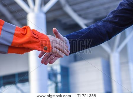 businessman handshaking with worker. Moment before handshake of suit and boilersuit. Business modern background