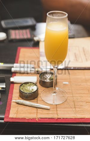 Alcoholic beverage in focus on table place mat near cannibus and related accessories.