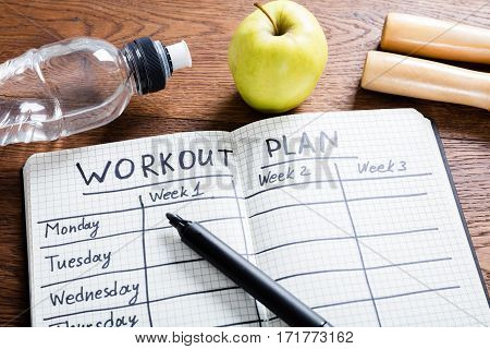High Angle View Of A Workout Plan In Notebook At Wooden Desk