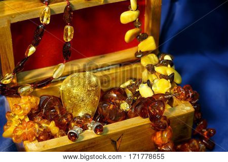 A lot of jewelry from authentic Baltic amber with a radiant big pendant in the center in wooden chest on a blue background satin.
