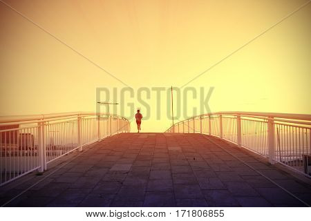 Woman running crossing a bridge next to the beack at sunset. Empty copy space for Editor's text.