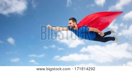freedom, power, motion and people concept - happy man in red superhero cape flying in air over blue sky and clouds background
