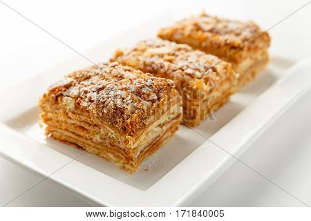 French Napoleon Cake of puff pastry with sour cream on a white plate close-up. Nutritious dessert. Selected Focus.