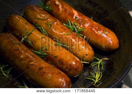 Cooked sausages with rosemary in a skillet.