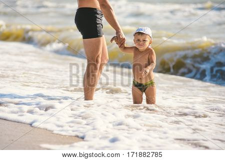 father and son go swim at beach. A child afraid to go into the water