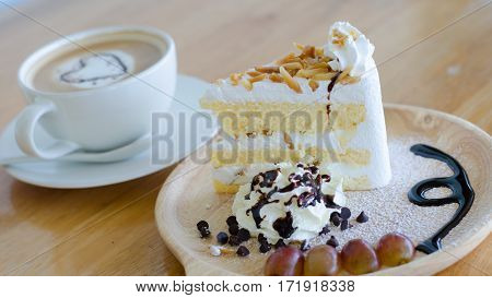 Closeup almond cake and coffee cup with heart shape latte art on wood table