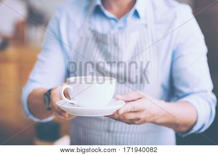 Thats for you. Close up of cup of coffee in hands of pleasant waiter holdign it while serving the guests