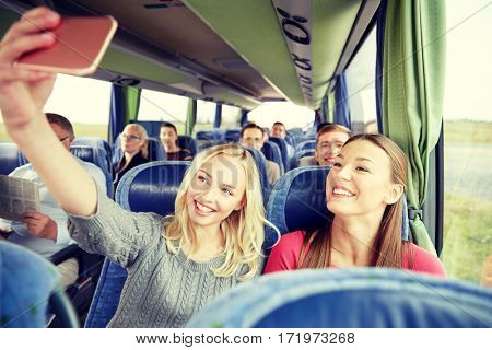 transport, tourism, road trip and people concept - happy young women or friends in travel bus taking selfie by smartphone