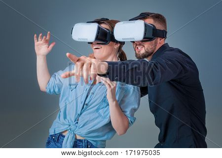 Excited young man and woman having fun with a VR glasses. Emotions couples. Gray background