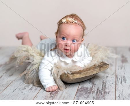 Adorable newborn baby girl with headband lying on fluffy rug and looking aside with curiosity. Cute infant girl with beautiful blue eyes lying on tummy