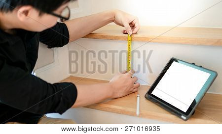 Young Asian Worker Using Tape Measure For Measuring Riser And Thread On Stair In The House. Writing 