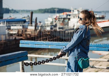 Fun Teenage Girl In Blue Denim Dress Is Walking In River Station. Young Cheerful Child Piddle In Riv