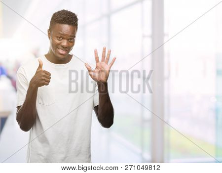 Young african american man wearing white t-shirt showing and pointing up with fingers number six while smiling confident and happy.