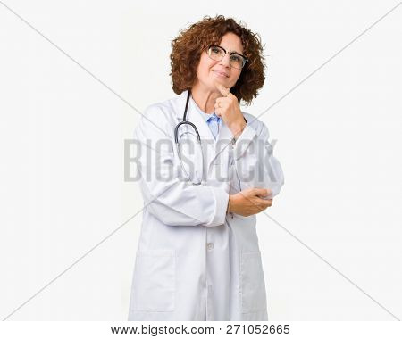 Middle ager senior doctor woman over isolated background looking confident at the camera with smile with crossed arms and hand raised on chin. Thinking positive.