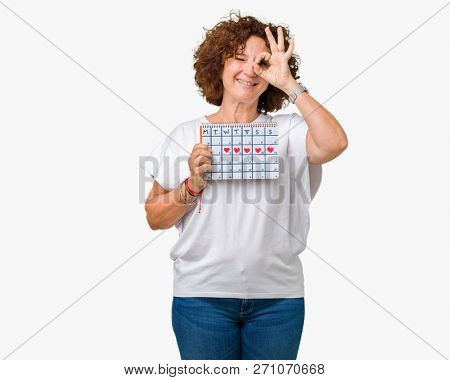 Middle ager senior woman holding menstruation calendar over isolated background with happy face smiling doing ok sign with hand on eye looking through fingers