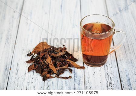 Cup Of Hot Black Tea And Dried Tea Leaves On Wooden Table