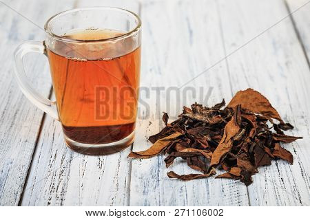 Cup Of Hot Black Tea And Dried Tea Leaves On Wooden Table