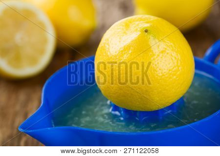 Lemon Half On Blue Lemon Or Citrus Squeezer With Lemons In The Back, Photographed On Wood (selective
