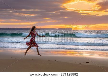 Running Along The Beach In Wet Sand From Tidal Waves, The Sky Full Of Orange And Yellow Sunbeams Shi