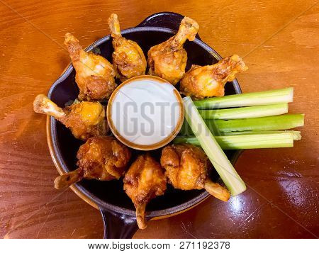 Delicoius Chicken Wings And Celery Sticks Placed In A Round Plate With A Small Bow Of White Sauce In